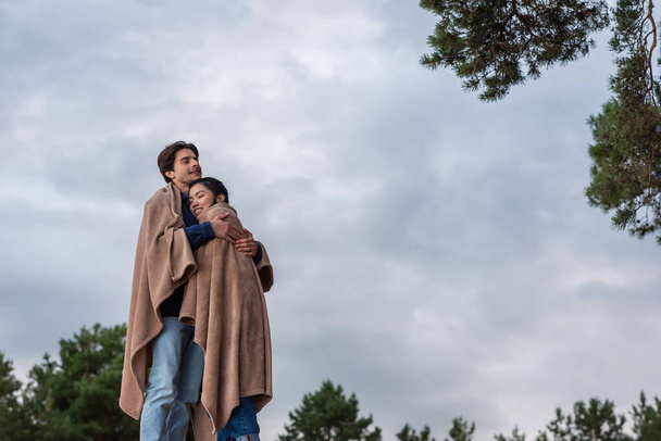 Man hugging asian girlfriend in blanket outdoors  - Fotó, kép