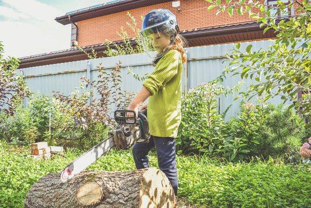 a girl child in a helmet with an electric saw saws a log - 写真・画像