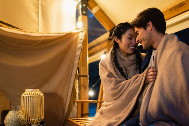 Asian woman hugging boyfriend in blanket on terrace of glamping house - Photo, Image