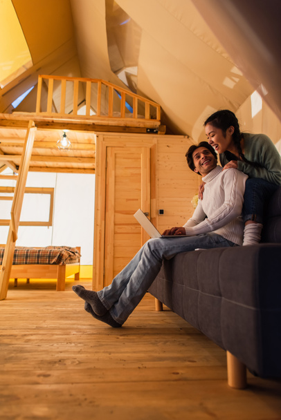 Cheerful interracial couple using laptop in wooden glamping house  - Photo, Image