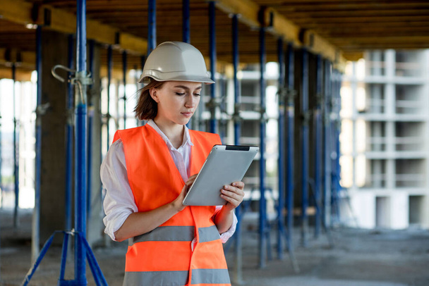 Female construction engineer. Architect with a tablet computer at a construction site. Young Woman looking, building site place on background. Construction concept. - Valokuva, kuva