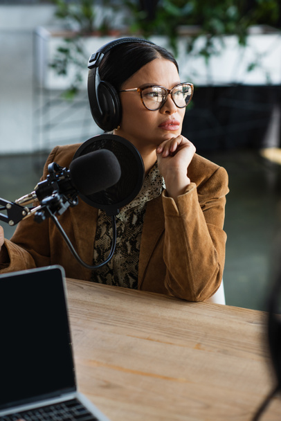 pensivo asiático mulher no óculos e fones de ouvido olhando afastado no podcast studio  - Foto, Imagem