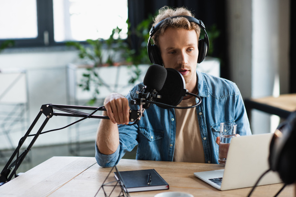 young radio host in headphones touching microphone while talking during podcast - Foto, Bild