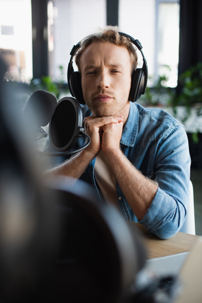 host de radio enfocado en auriculares inalámbricos cerca del micrófono en el estudio  - Foto, Imagen