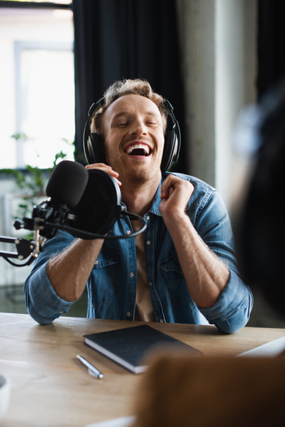 Радостный радиоведущий смеется возле микрофона в студии  - Фото, изображение