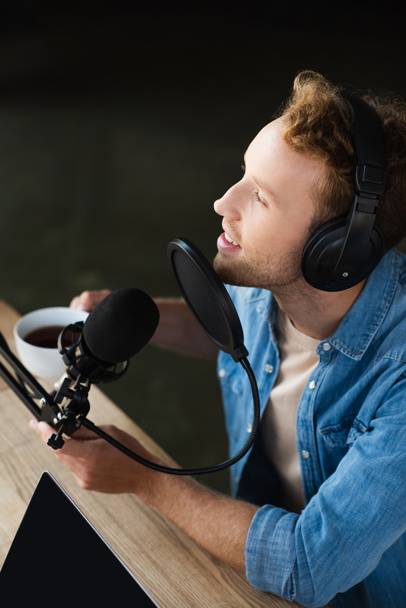 magas látószögű kilátás pozitív rádió host a fejhallgató kezében csésze kávé podcast stúdióban  - Fotó, kép