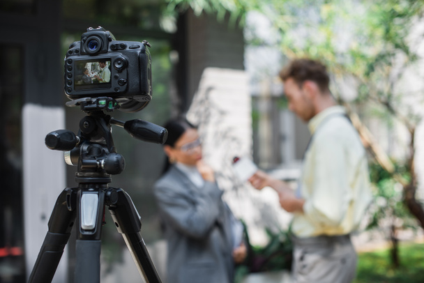 ψηφιακή φωτογραφική μηχανή με δημοσιογράφος κρατώντας μικρόφωνο, ενώ λαμβάνοντας συνέντευξη της ασιάτισσας επιχειρηματίας σε γυαλιά στην οθόνη - Φωτογραφία, εικόνα