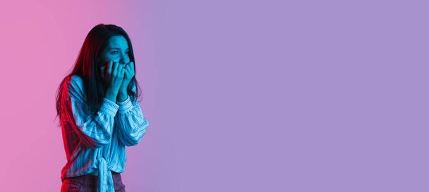 Portrait of young beautiful girl isolated over gradient pink purple background in neon lights. Scared facial expression. Flyer - Photo, Image