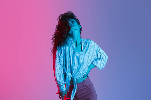 Portrét v pohybu mladé krásné dívky tanec izolované přes gradient růžové fialové pozadí v neonových světel - Fotografie, Obrázek