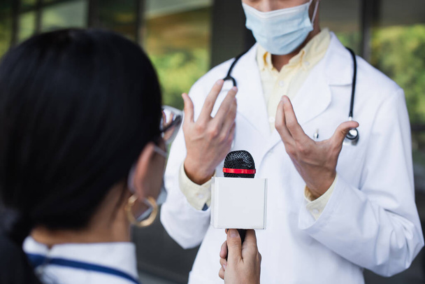 θολή γιατρός σε ιατρική μάσκα gesturing κατά τη διάρκεια της συνέντευξης  - Φωτογραφία, εικόνα