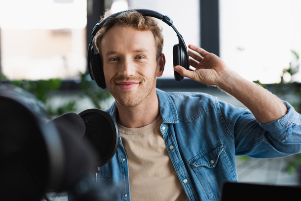 gelukkig influencer aanpassen van koptelefoon tijdens het maken van podcast in de studio - Foto, afbeelding