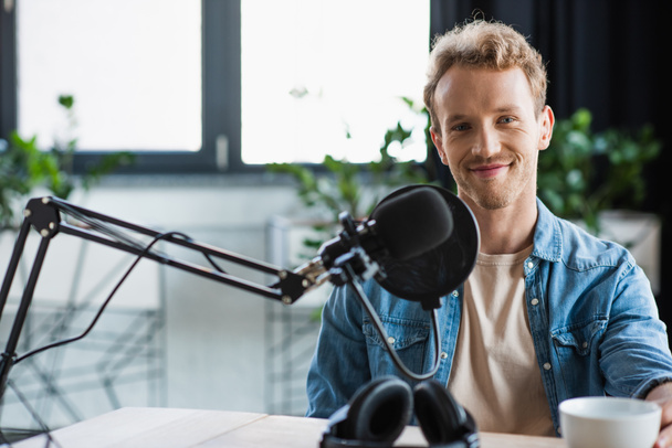 happy influencer looking at camera near microphone in studio - Foto, afbeelding