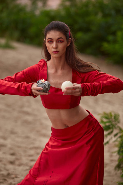 Ritual dance with candles in hands. Brunette woman in red costume for belly-dance is dancing on the beach - Foto, immagini