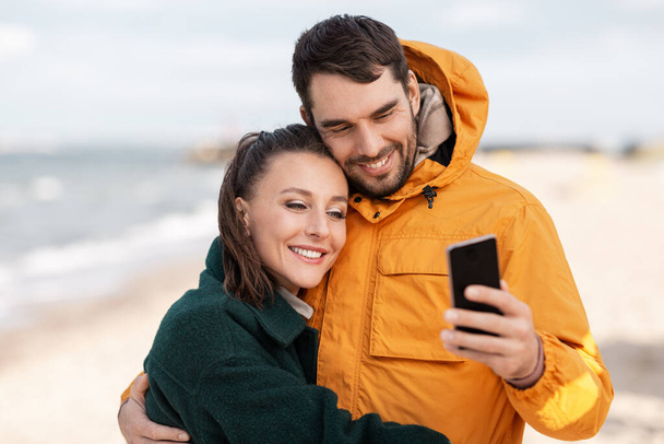 couple with smartphone on autumn beach - Foto, Imagem