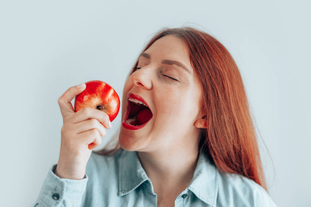 Gri arka planda kırmızı elma yiyen neşeli genç bir kadının portresi. Sağlıklı beslenme diyeti. Elma vitamini.. - Fotoğraf, Görsel