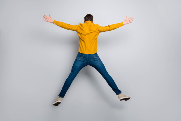 Full length body size rear back behind view of attractive free man jumping having fun isolated over grey color background - Фото, изображение