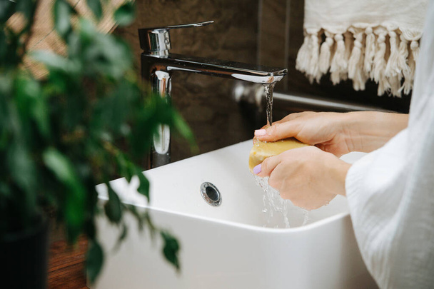Hands of a mature woman washing themselves with an eco soap block. She's standing in front of the sink in a bathroom. - Fotó, kép