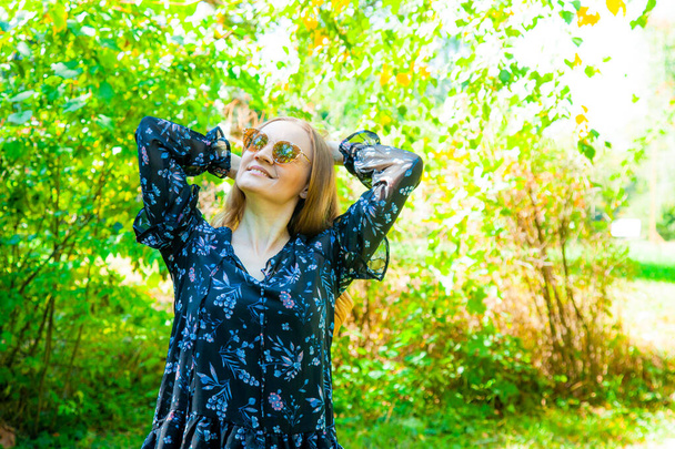Молода блондинка в чорній сукні з квітковим принтом в осінньому парку, сонячний день. Вулична мода, вуличний стиль. Зображення осіннього вбрання
 - Фото, зображення
