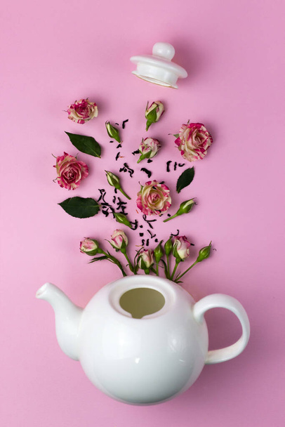 Creatieve lay-out met bloemen vliegen uit de theepot. Ketel en rozen. Roze achtergrond. Zicht van bovenaf. Plat gelegd. Theetijd concept. - Foto, afbeelding