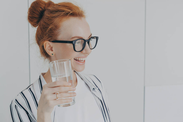Жаждущая женщина с рыжими волосами расчесывается в булочки напитки еще вода предотвращает обезвоживание держит стекло - Фото, изображение