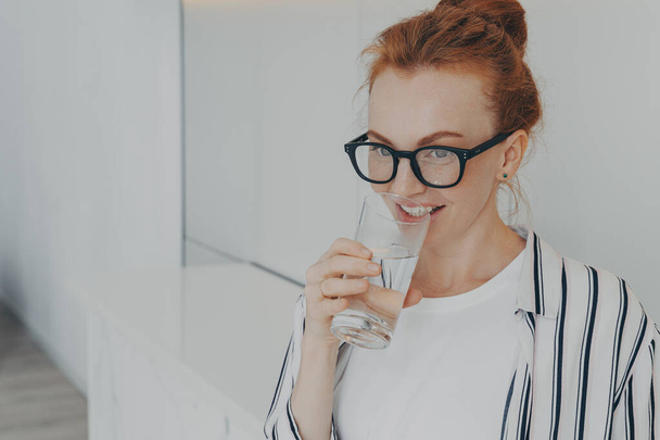 Happy healthy beautiful young redhead woman drinking water in morning at home - Fotó, kép