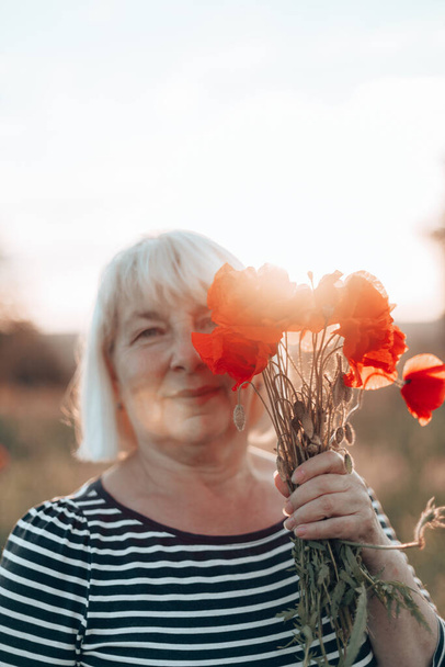 Caucasian woman hand holding a bouquet of poppy flower on meadow background at sunset - Fotografie, Obrázek
