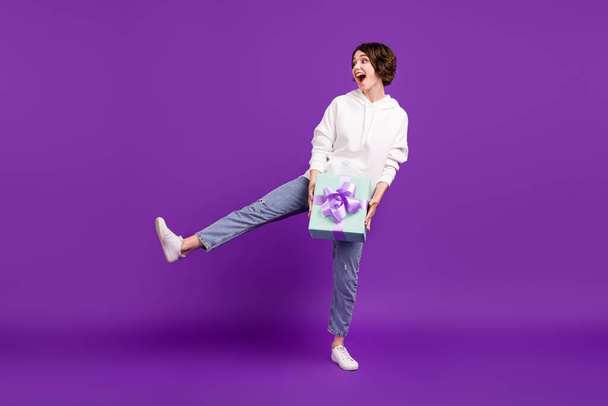 Full size photo of young excited crazy good mood girl fooling around hold birthday present isolated on violet color background - Фото, изображение
