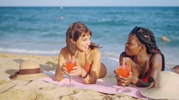 Twee jonge multiraciale meisjes liggend op zandstrand - Video