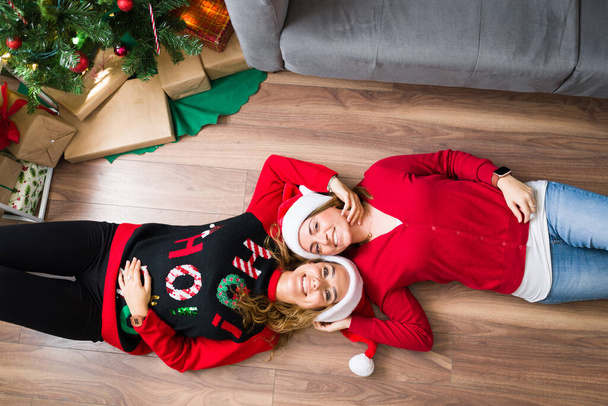 High angle of a two gay women resting on the living room floor while smiling and looking at the camera  - Photo, Image