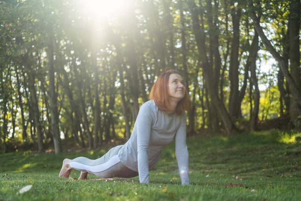 Millennial szczupły imbir kobieta robi jogę odkryty na łonie natury w mieście jesienią słoneczny dzień na wschodzie słońca. - Zdjęcie, obraz