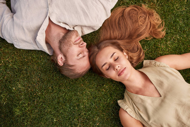 Top view of relaxed young couple lying together on green grass with eyes closed - Photo, image