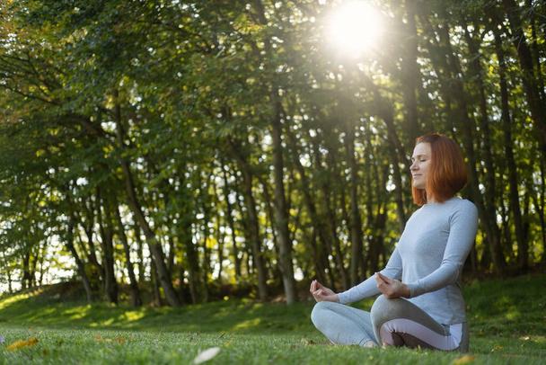 Millennial sottile zenzero donna facendo yoga all'aperto sulla natura in città in autunno giornata di sole all'alba. - Foto, immagini