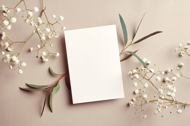 Wedding invitation card mockup with natural eucalyptus and white gypsophila twigs. Blank card mockup on beige background. - Foto, afbeelding