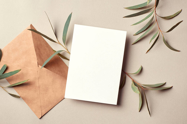 Greeting or invitation card mockup with envelope and eucalyptus twigs. Card mockup with copy space on beige background. - Foto, immagini