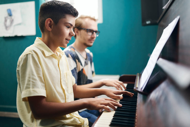 Улыбающийся мальчик играет на пианино со своим учителем - Фото, изображение