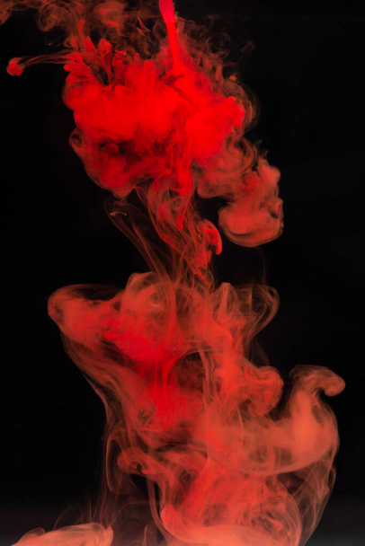 Red paint dissolves in water on a black background. Watercolor paint in water - Foto, Bild