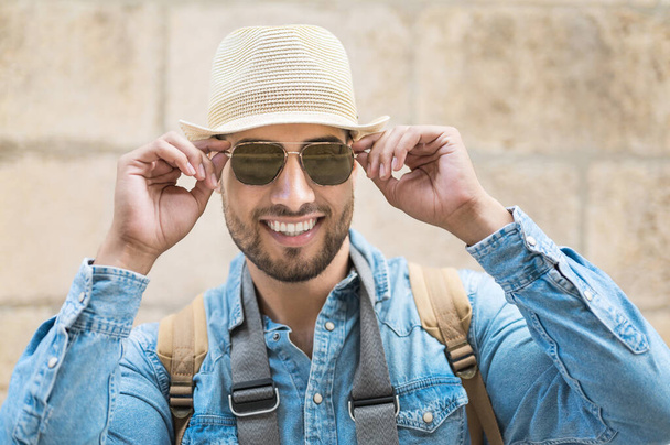 スタイリッシュな旅行者ひげを生やした男で帽子をかぶってカメラを見て、旅行とさまよう欲望の概念. - 写真・画像