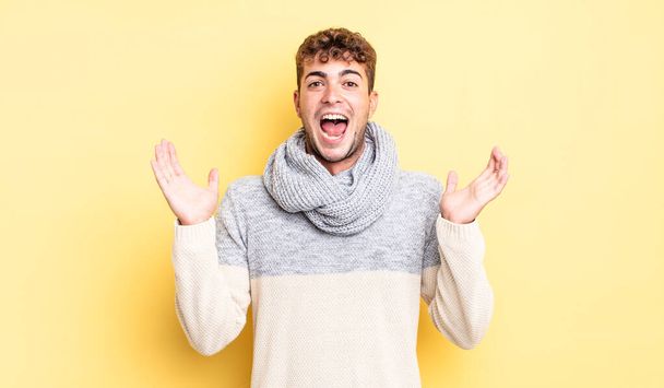 young handsome man looking happy and excited, shocked with an unexpected surprise with both hands open next to face - 写真・画像