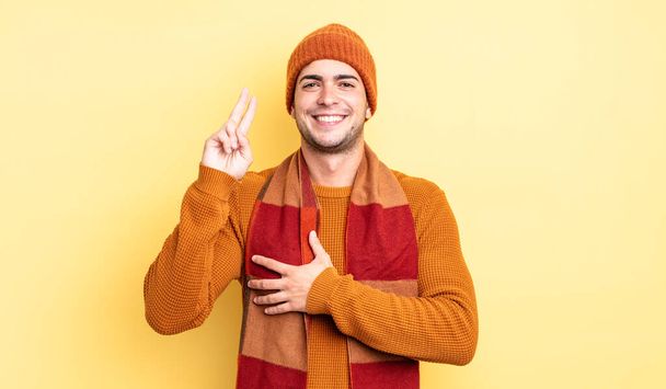 young handsome man looking happy, confident and trustworthy, smiling and showing victory sign, with a positive attitude - Foto, Imagen