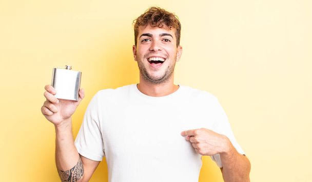 young handsome man feeling happy and pointing to self with an excited. alcohol flask concept - 写真・画像