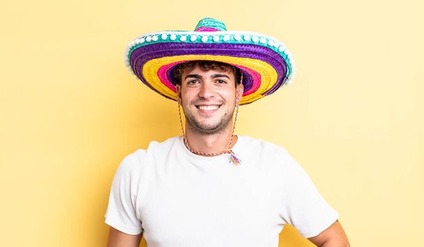 若いハンサムな男が喜んで笑顔で手を腰と自信を持って。メキシコの帽子のコンセプト - 写真・画像