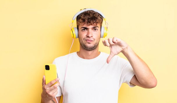 young handsome man feeling cross,showing thumbs down. headphones and smartphone concept - Foto, immagini