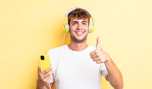 young handsome man feeling proud,smiling positively with thumbs up. headphones and smartphone concept - Fotoğraf, Görsel