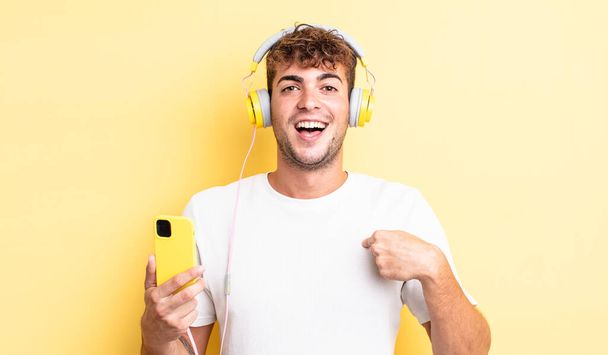 young handsome man feeling happy and pointing to self with an excited. headphones and smartphone concept - Photo, Image