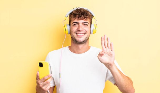 young handsome man smiling and looking friendly, showing number four. headphones and smartphone concept - Photo, Image