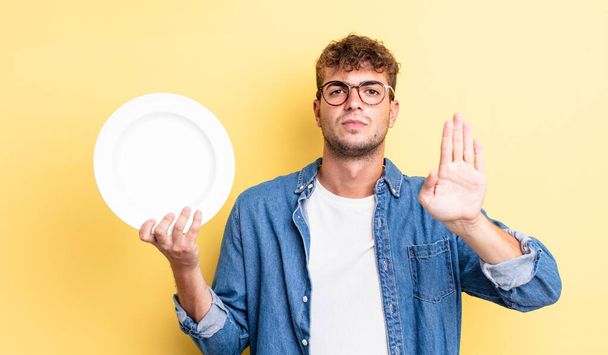 young handsome man looking serious showing open palm making stop gesture. empty dish concept - Foto, immagini