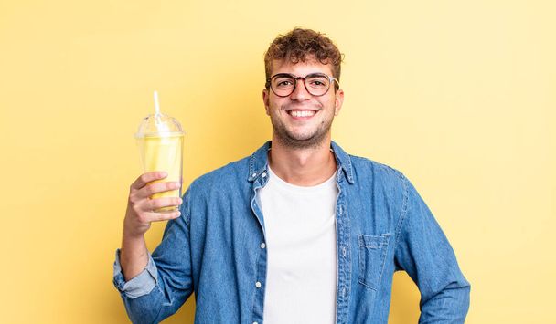young handsome man smiling happily with a hand on hip and confident. milkshake concept - Foto, Imagen