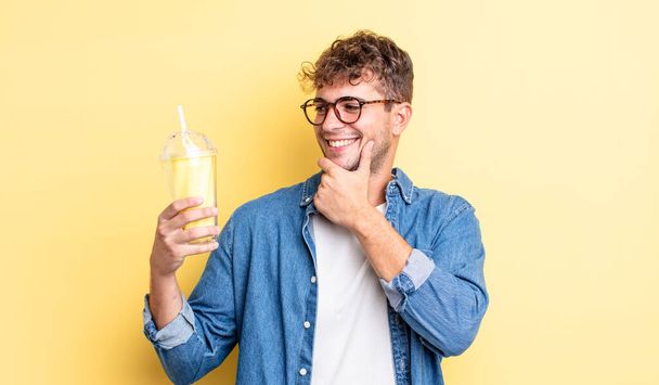 young handsome man smiling with a happy, confident expression with hand on chin. milkshake concept - Φωτογραφία, εικόνα