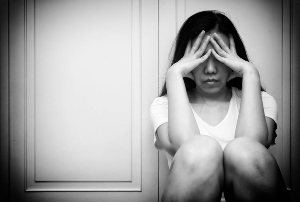 Ασιάτισσα γυναίκα με τα χέρια στο πρόσωπό της, κλαίει ενώ κάθεται στο πάτωμα, αισθάνεται λυπημένη κουρασμένη και υποφέρει από μείζονα καταθλιπτική διαταραχή. Ψυχική υγεία ή ψυχολογική έννοια. Ασπρόμαυρος τόνος - Φωτογραφία, εικόνα