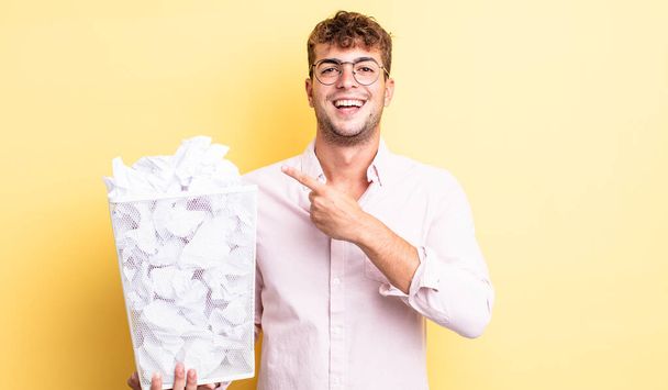 young handsome man looking excited and surprised pointing to the side. paper balls trash concept - Foto, Imagem